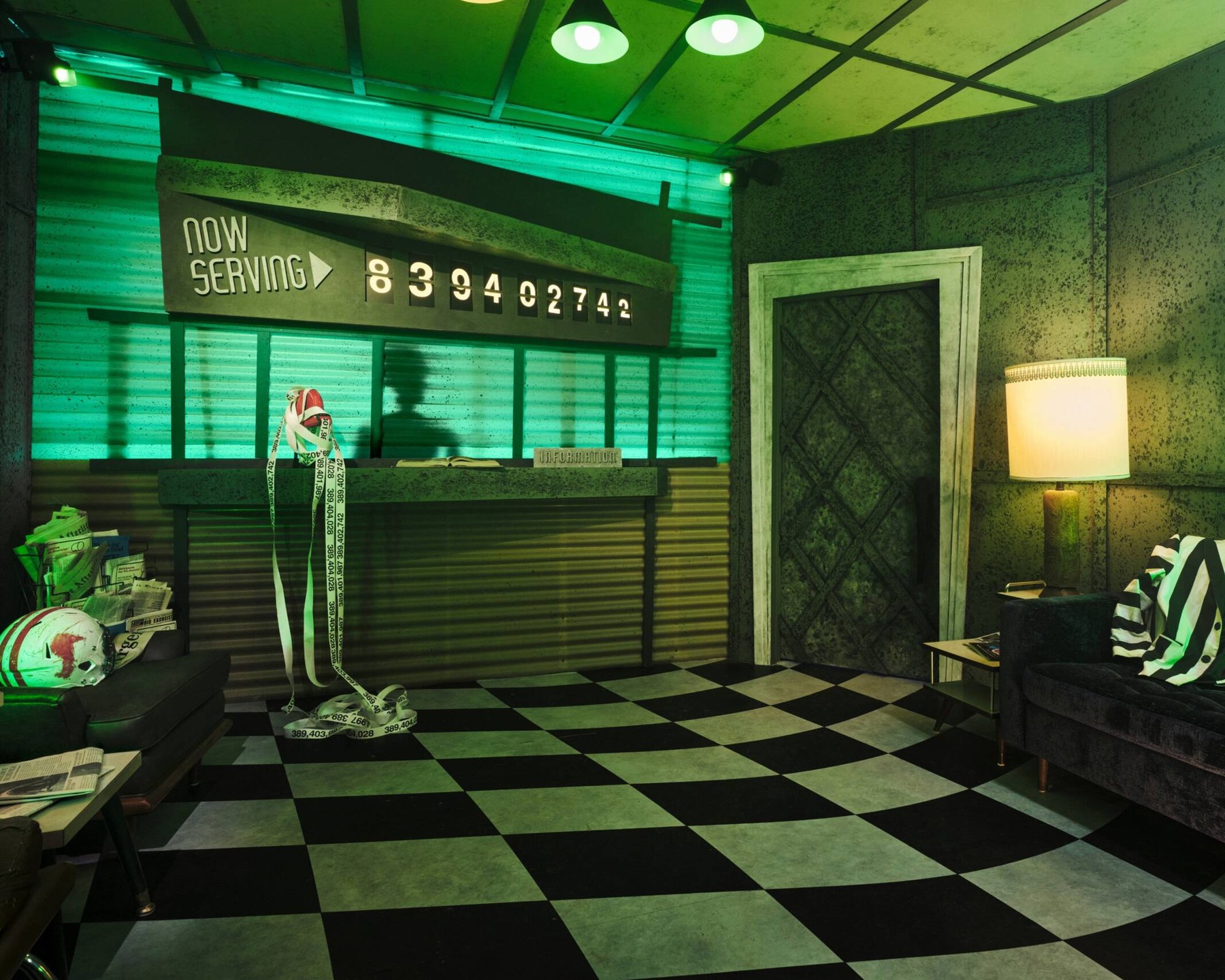 The green-lit Netherworld waiting room with checkerboard floor and Now Serving sign