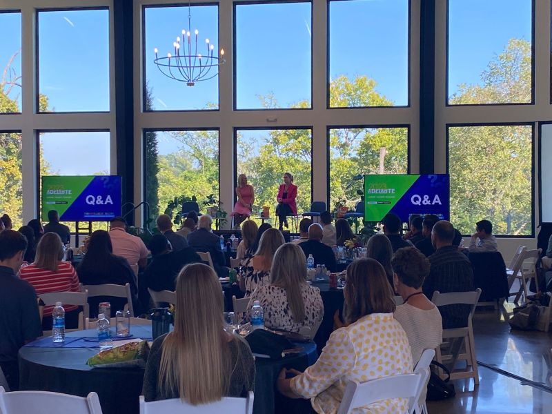 Q&A session at the Adelante summit with speakers on stage in front of floor-to-ceiling windows