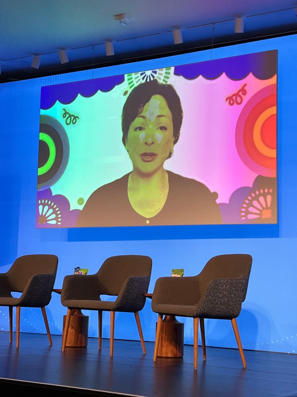 Virtual keynote speaker on the large stage screen framed by Por La Cultura artwork