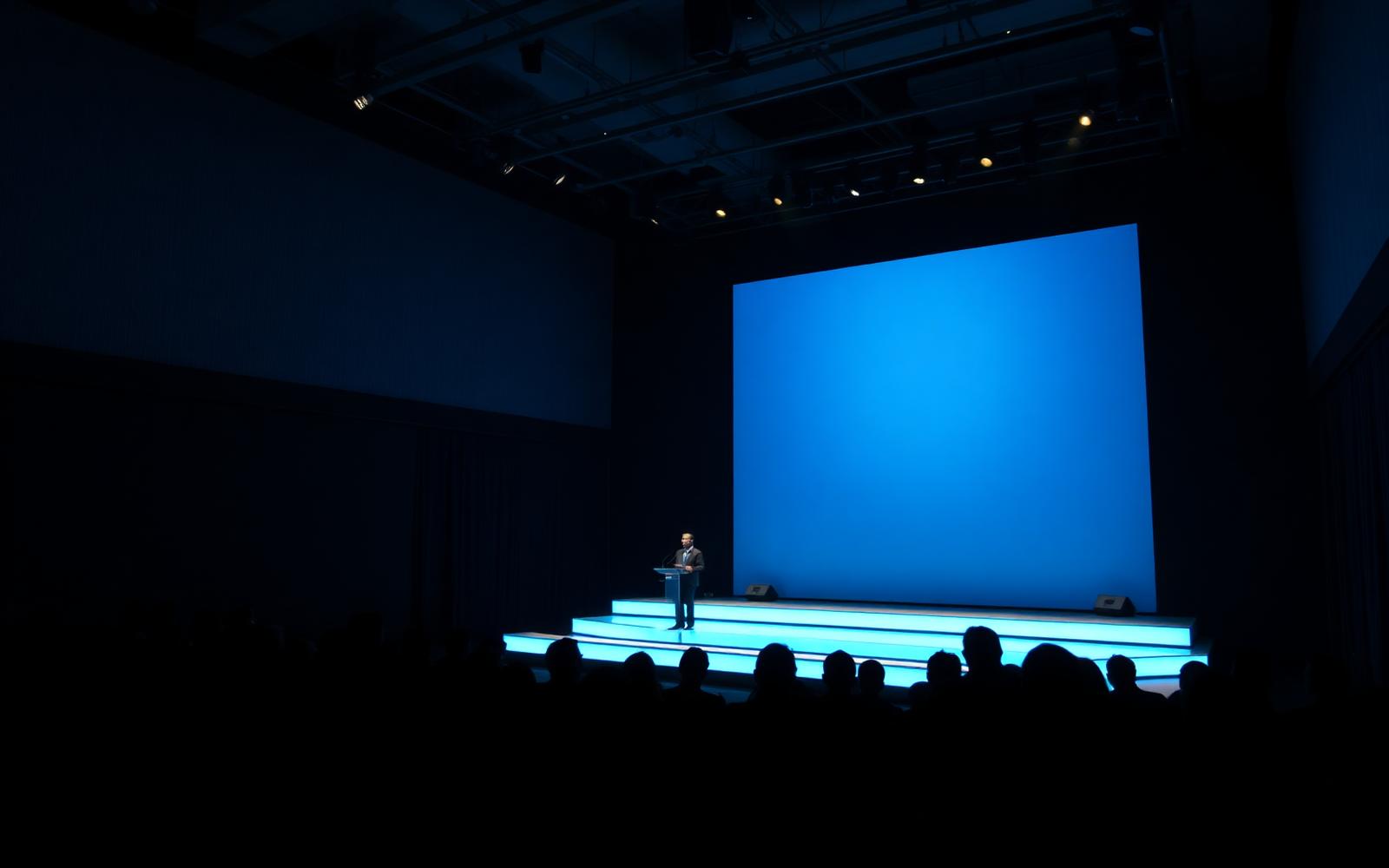Corporate summit stage with a large blue screen and seated audience