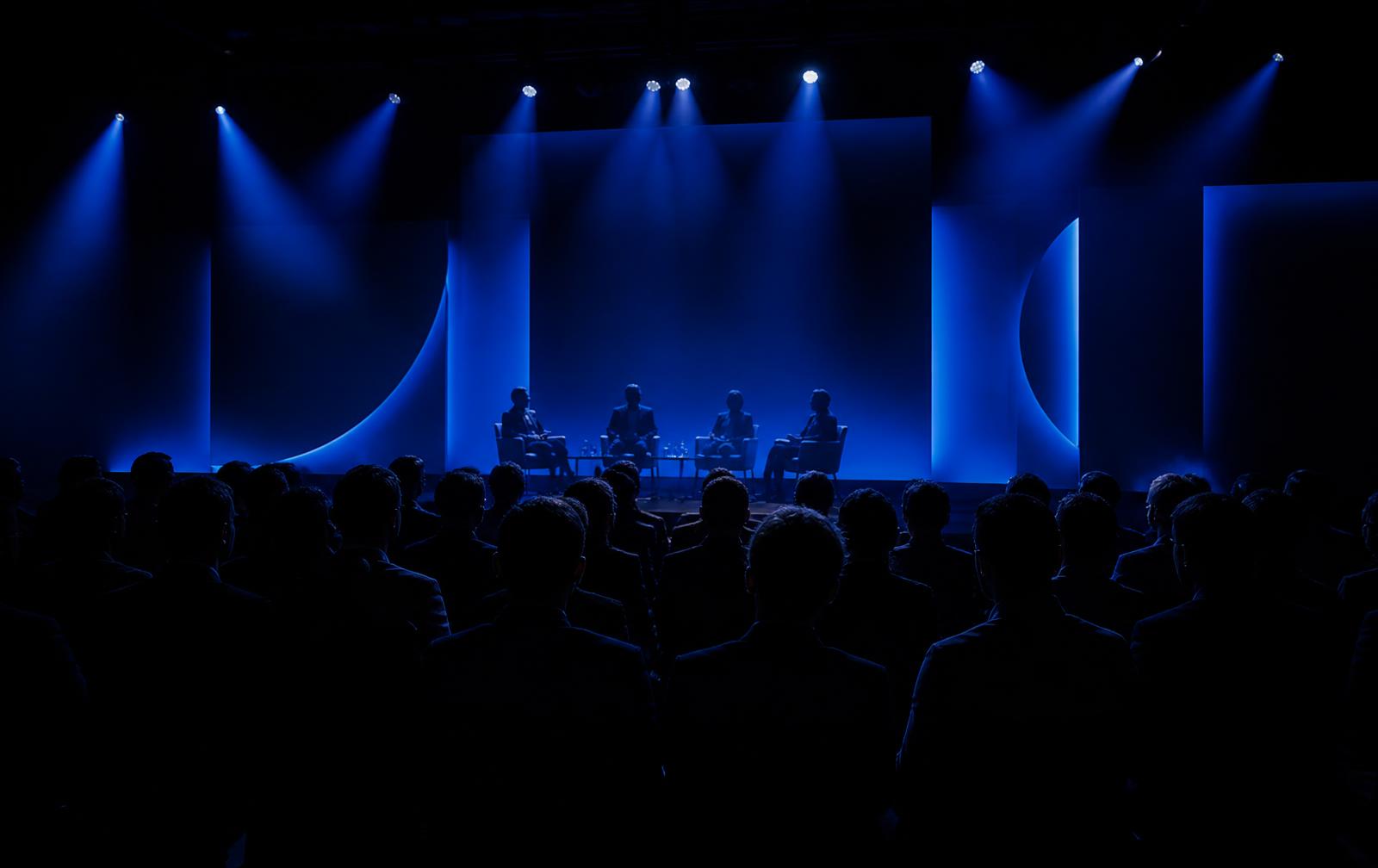 Executive summit stage under blue lighting with a seated audience in silhouette