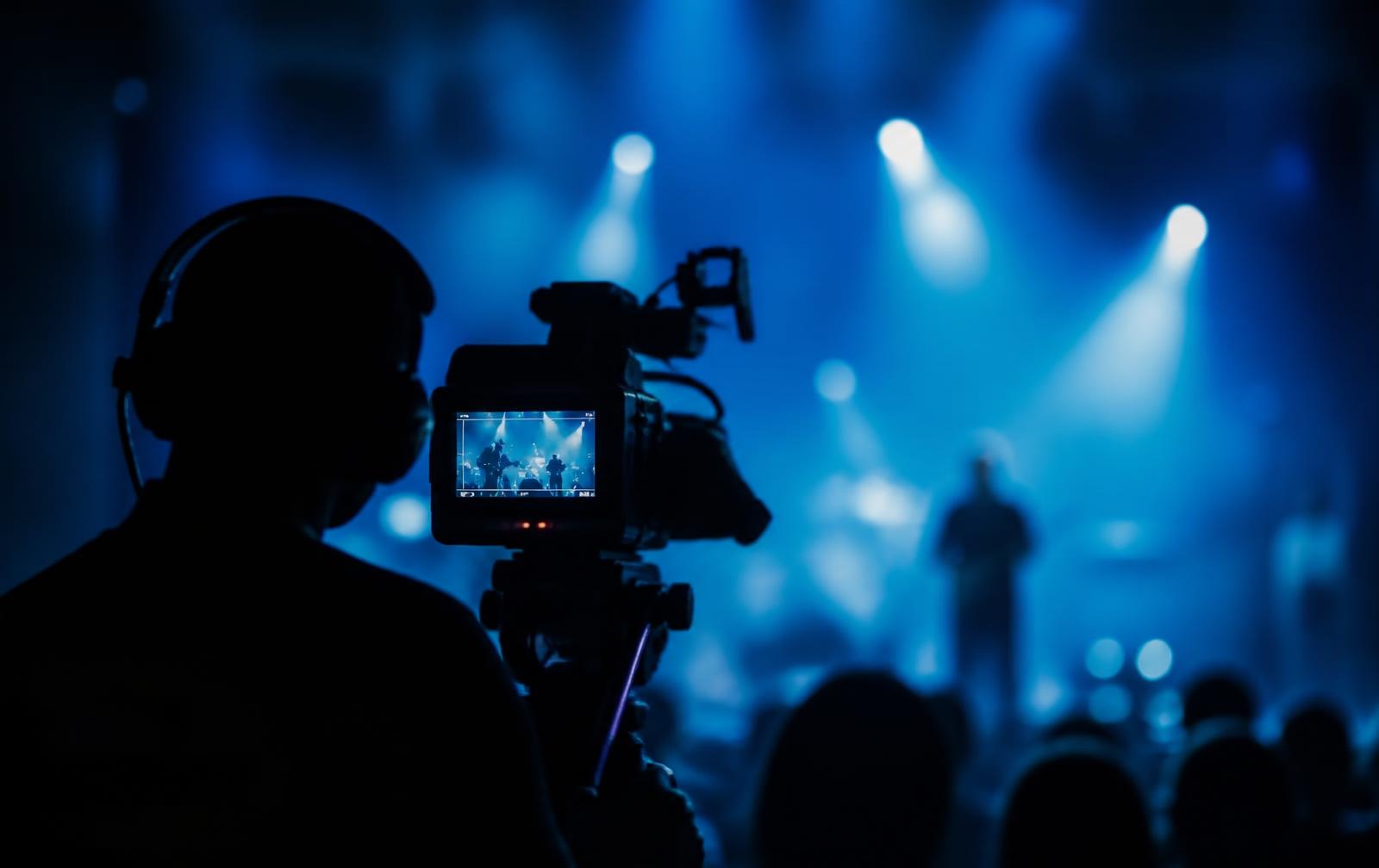 Camera operator filming a live stage moment lit in blue